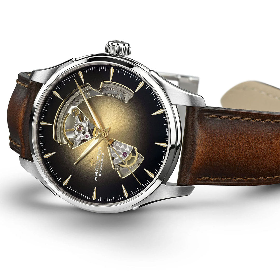 The Hamilton Jazzmaster Open Heart Auto 40mm by Hamilton Watch features a brown leather strap, stainless steel case, and an open-heart black and gold gradient dial that reveals the movement. The watch is positioned at a slight angle.