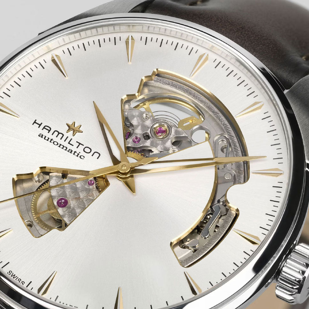 Close-up of the Hamilton Jazzmaster Open Heart Auto 40mm Watch by Hamilton Watch, featuring a silver dial, gold hands and markers, open-heart H-10-S automatic movement, brown leather strap, and polished steel case.