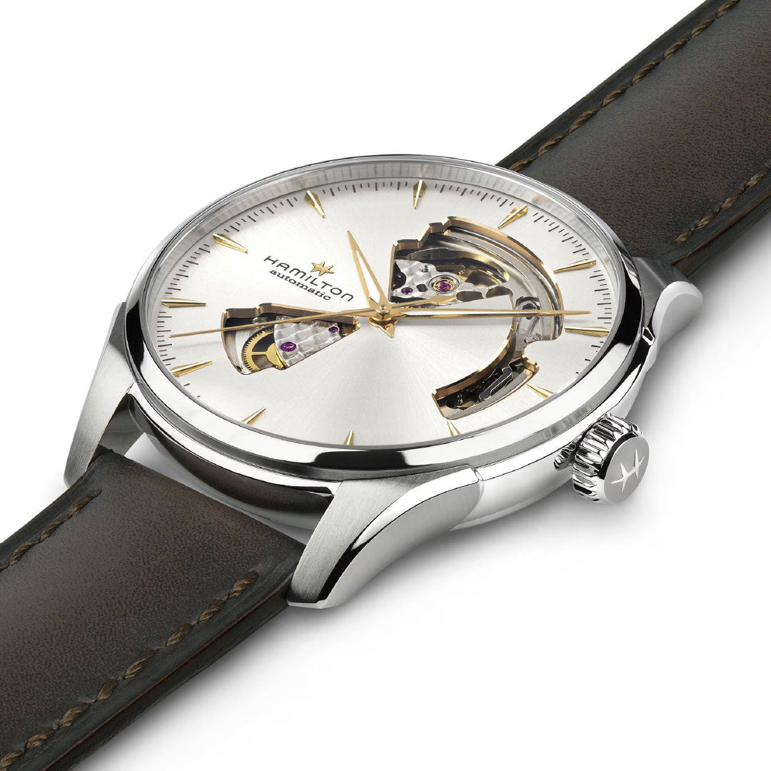 The Hamilton Jazzmaster Open Heart Auto 40mm Watch by Hamilton Watch features a silver dial, exposed automatic movement, gold accents, brown leather strap, and a stainless steel case with a crown embossed with the Hamilton logo.