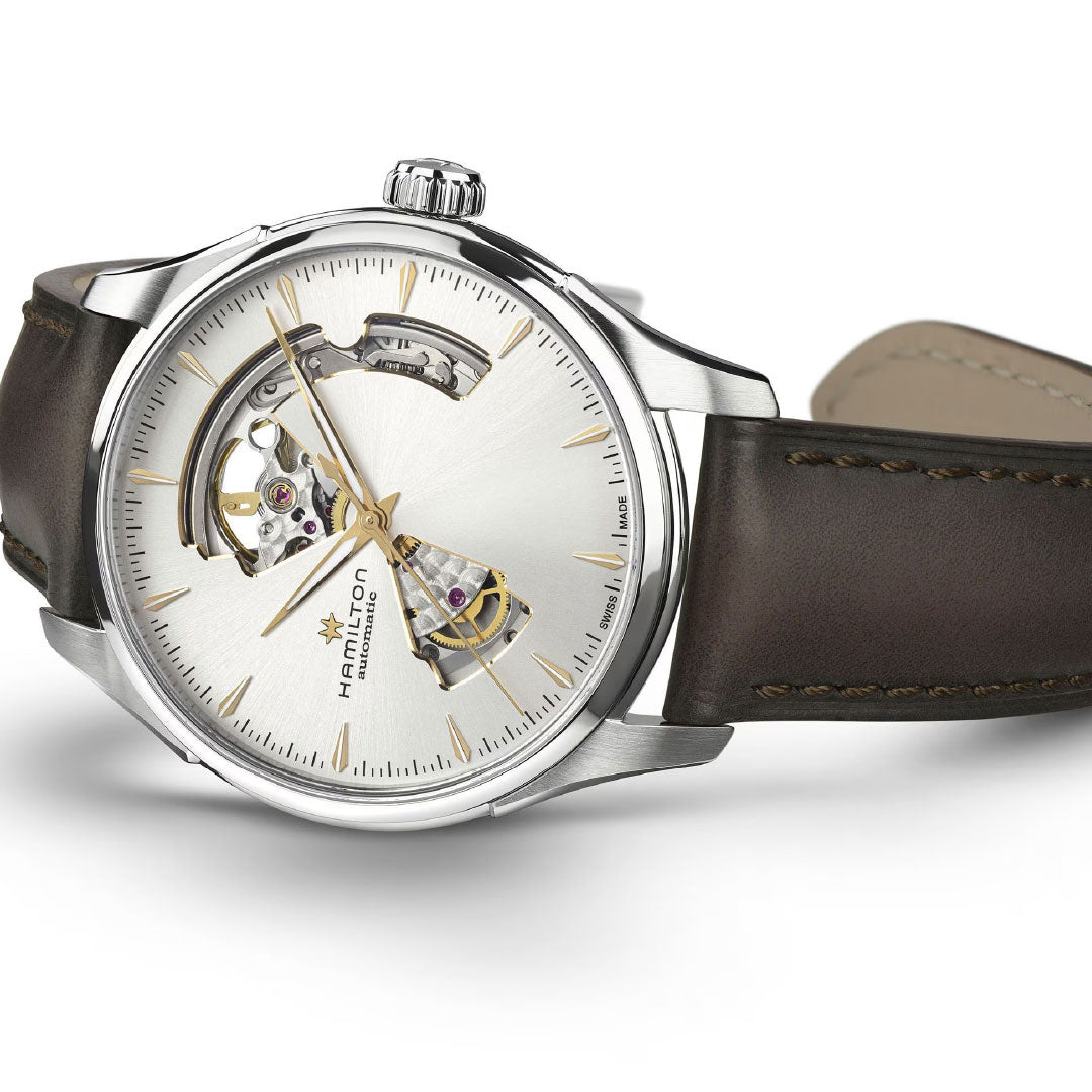 The Hamilton Jazzmaster Open Heart Auto 40mm Watch by Hamilton Watch features a silver case, brown leather strap, partially open dial displaying the H-10-S automatic movement, gold markers and hands, shown on a white surface.
