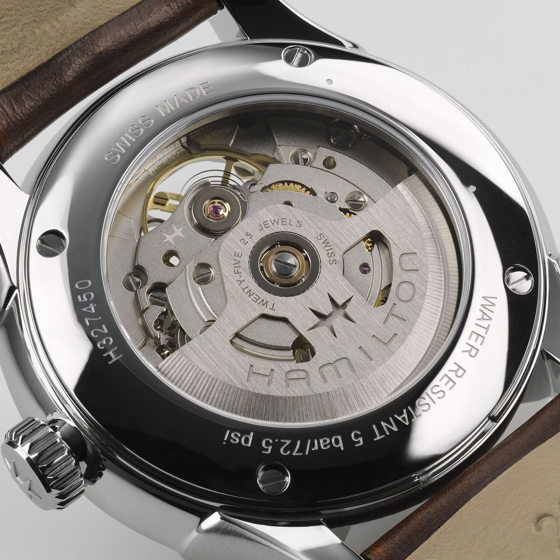 Close-up of the Hamilton Jazzmaster Open Heart Auto 40mm Watch by Hamilton Watch, showing its transparent caseback with visible H-10-S automatic movement, metal gears, engraved details, and a glimpse of the brown leather strap.