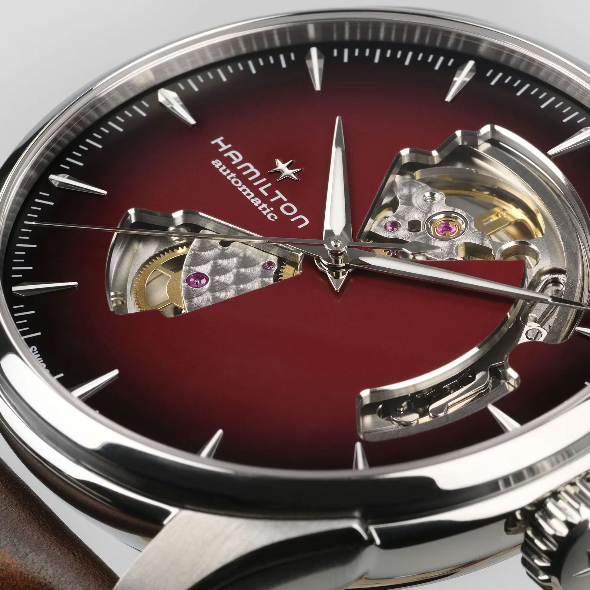 Close-up of a Hamilton Watch Jazzmaster Open Heart Auto 40mm wristwatch featuring a deep red dial, silver hour markers, and cutouts that display the automatic movement beneath the face.