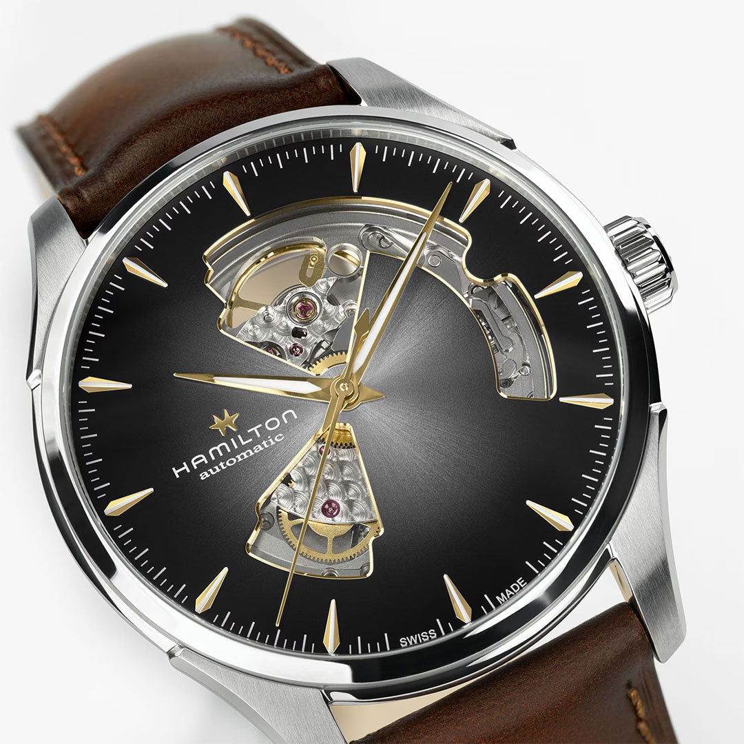 A close-up of the Hamilton Jazzmaster Open Heart Auto 40mm Watch by Hamilton Watch, featuring a black dial, gold hour markers, open-heart design displaying the movement, and a brown leather strap for a refined look.