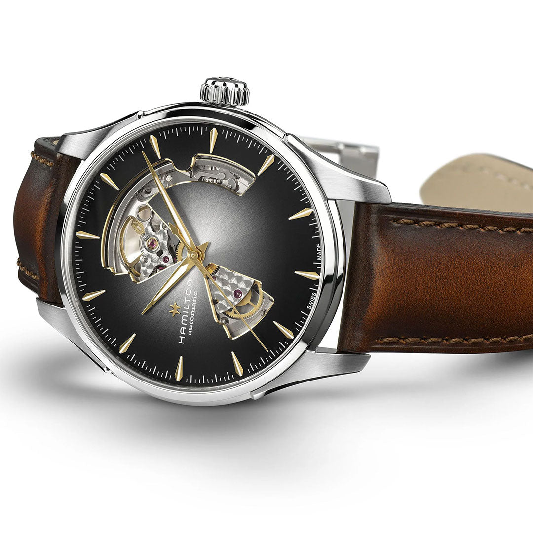A close-up of the Hamilton Jazzmaster Open Heart Auto 40mm Watch by Hamilton Watch, featuring a brown leather strap, silver case, black dial with gold hour markers, and a stylish open-heart design revealing its mechanical movement.