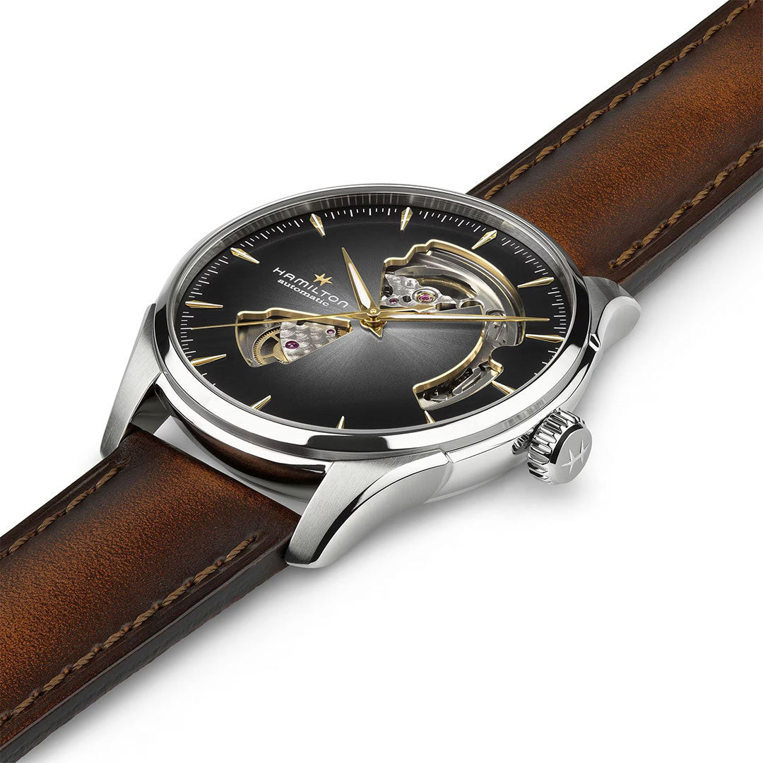 The Hamilton Jazzmaster Open Heart Auto 40mm Watch by Hamilton Watch features a brown leather strap, silver case, black dial with gold hour markers, and open cutout sections that reveal its internal gears.