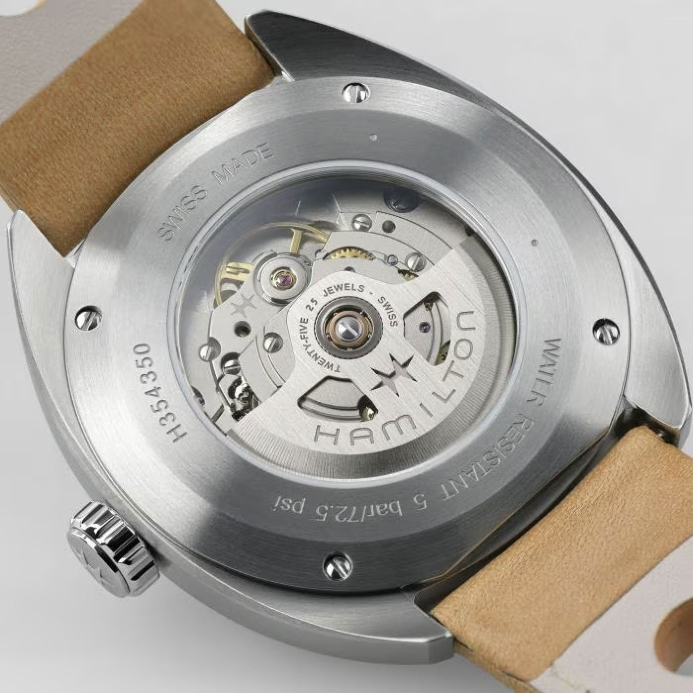 Close-up of the wristwatch back reveals an exposed mechanical movement. The Hamilton American Classic Pan Europ Day Date Auto 42mm Watch by Hamilton Watch features a stainless steel casing with visible gears and "Hamilton" engraved on the rotor. It is complemented by a beige leather strap.