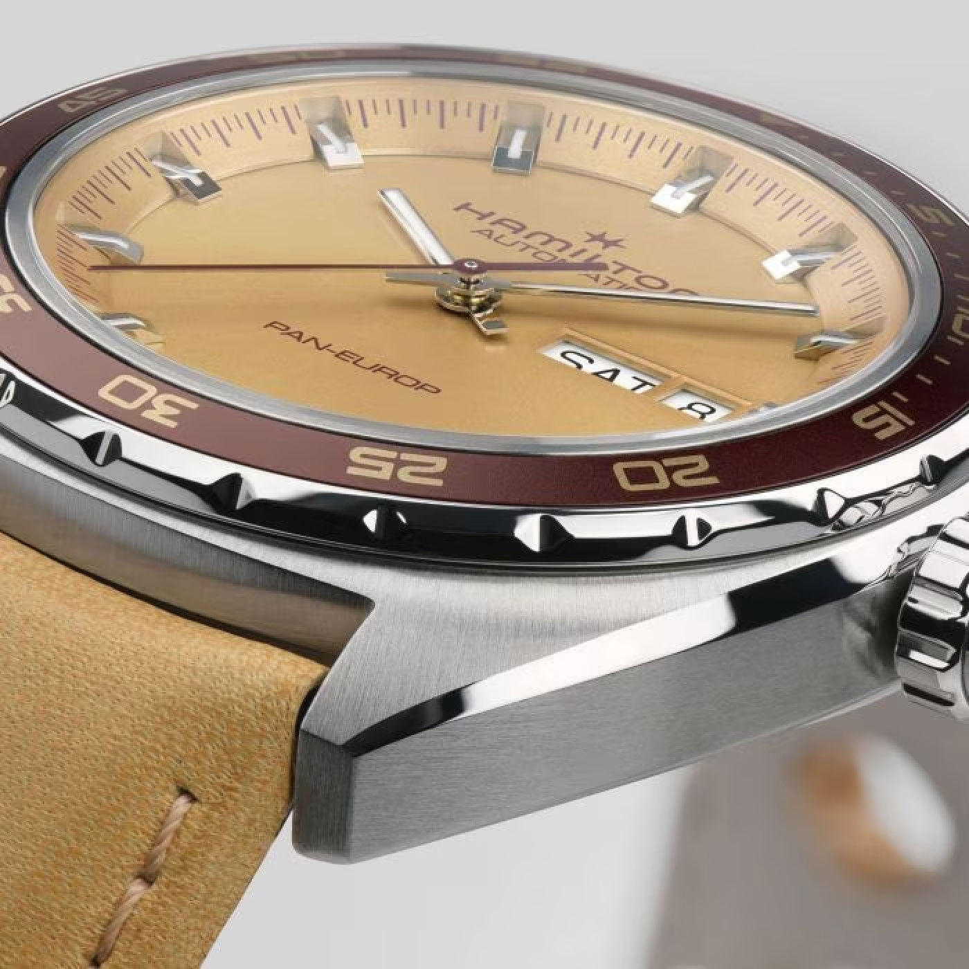 Detailed image of the Hamilton American Classic Pan Europ Day Date Auto 42mm Watch, showcasing its beige dial with silver markers. The timepiece features a brown bezel, "Hamilton Watch" branding, and displays both the date and day. It is attached to a beige leather strap and comes with a stainless steel case equipped with a crown on the side.