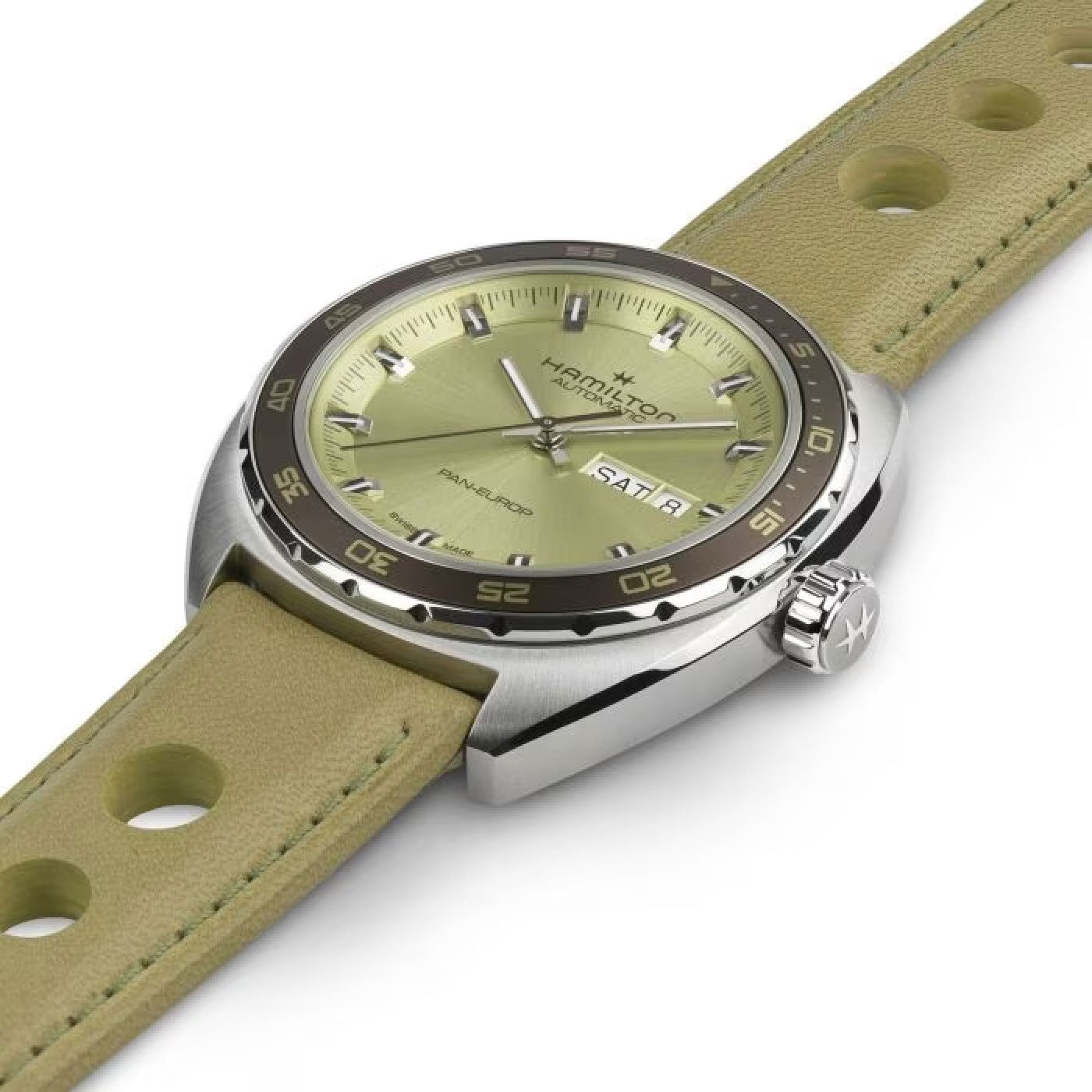 The Hamilton American Classic Pan Europ Day Date Auto 42mm Watch from Hamilton Watch features a matching perforated leather strap and a watch face highlighted by a chrome bezel and detailing. Silver hands and markers are stylishly arranged on a sleek olive green background, exuding sophistication and style. The day and date are also displayed for added convenience.