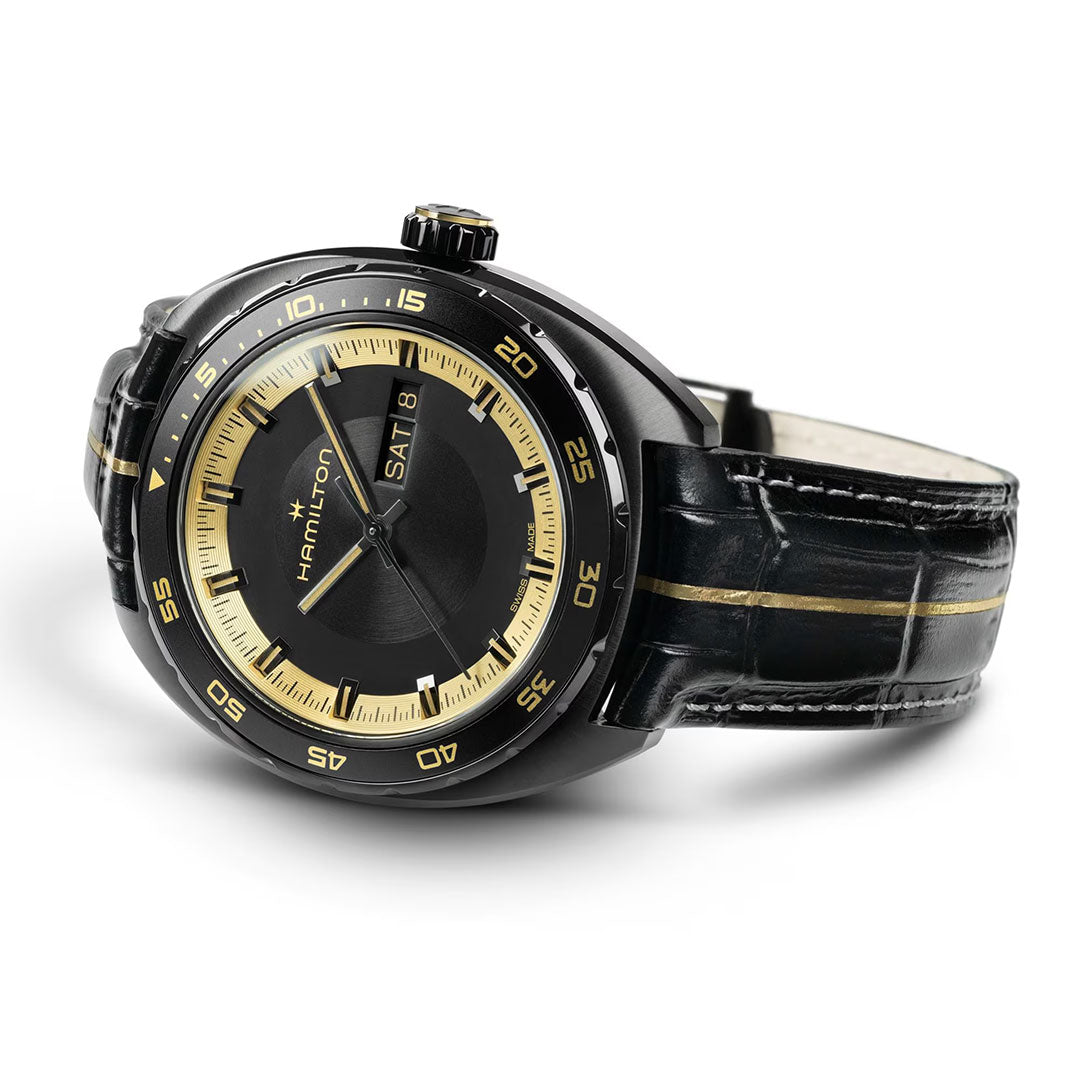 The Hamilton American Classic Pan Europ Resident Evil Requiem Limited Edition Auto 42mm Watch features black and gold styling, gold hands and hour markers, a day-date display at 3 o’clock, and a crocodile-pattern leather strap with a gold center stripe.