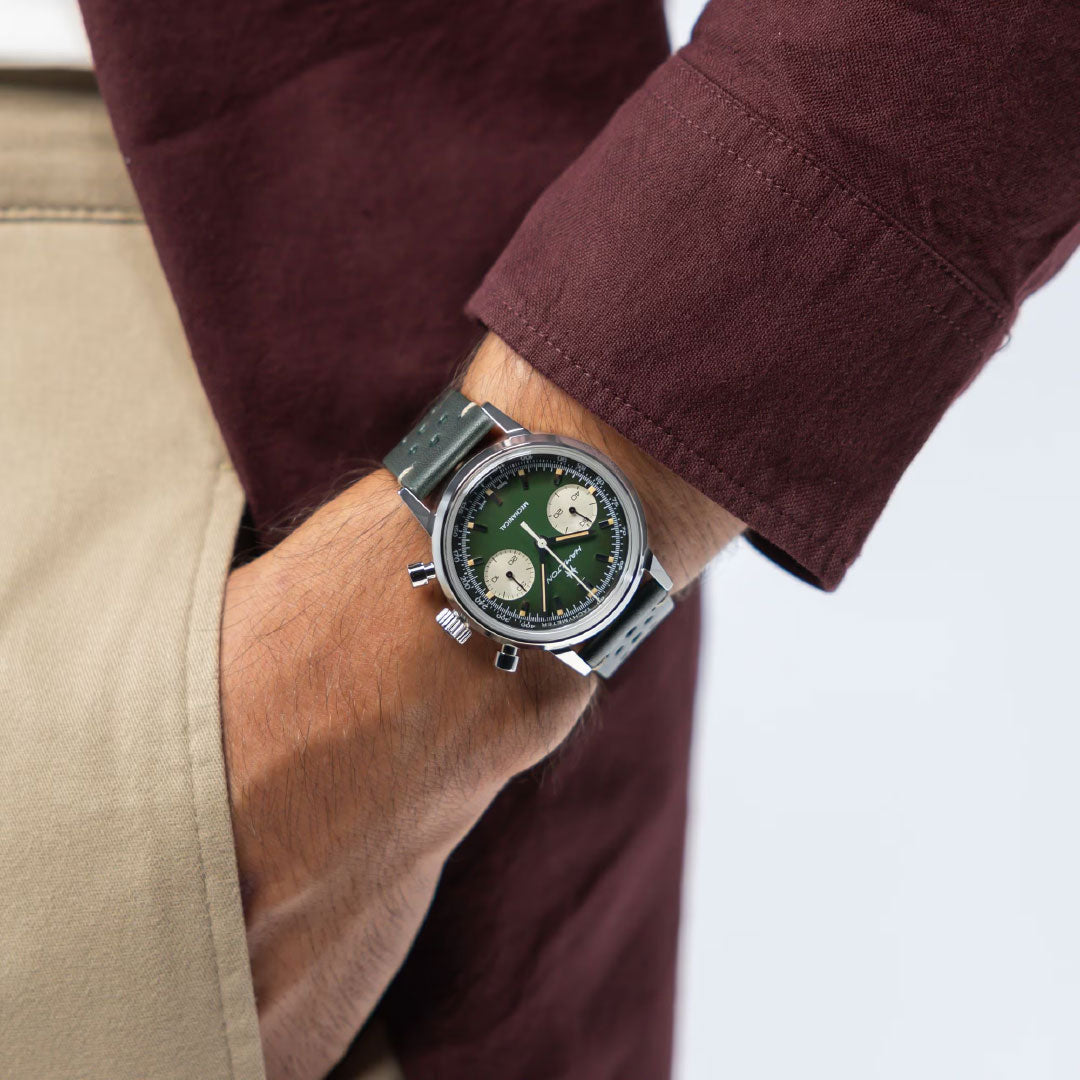 A person in tan pants and a maroon jacket slips a hand into their pocket, showcasing the Hamilton American Classic Intra-Matic Mechanical Chronograph H 40mm Watch by Hamilton Watch, featuring a green face and two white subdials.