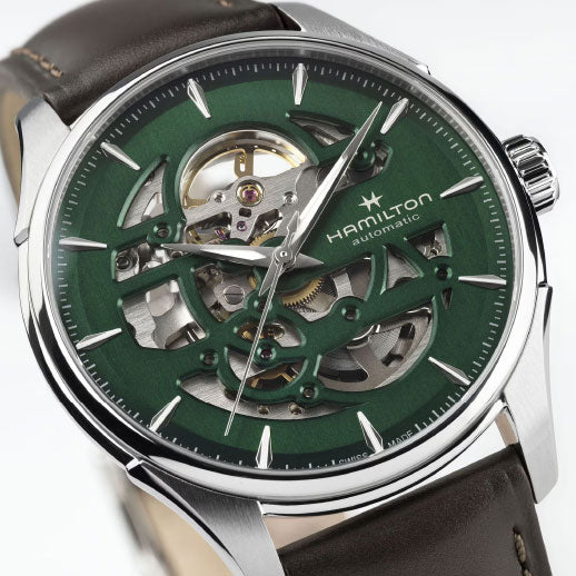 A close-up of the Hamilton Jazzmaster Skeleton Auto 40mm Watch by Hamilton Watch, featuring a green skeleton dial with exposed gears, Swiss automatic movement, silver case, and brown leather strap.