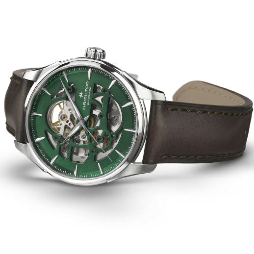 The Hamilton Jazzmaster Skeleton Auto 40mm Watch by Hamilton Watch showcases a green skeleton dial with Swiss automatic movement, silver markers and hands, 80-hour power reserve, and a dark brown leather strap, set against a white background.