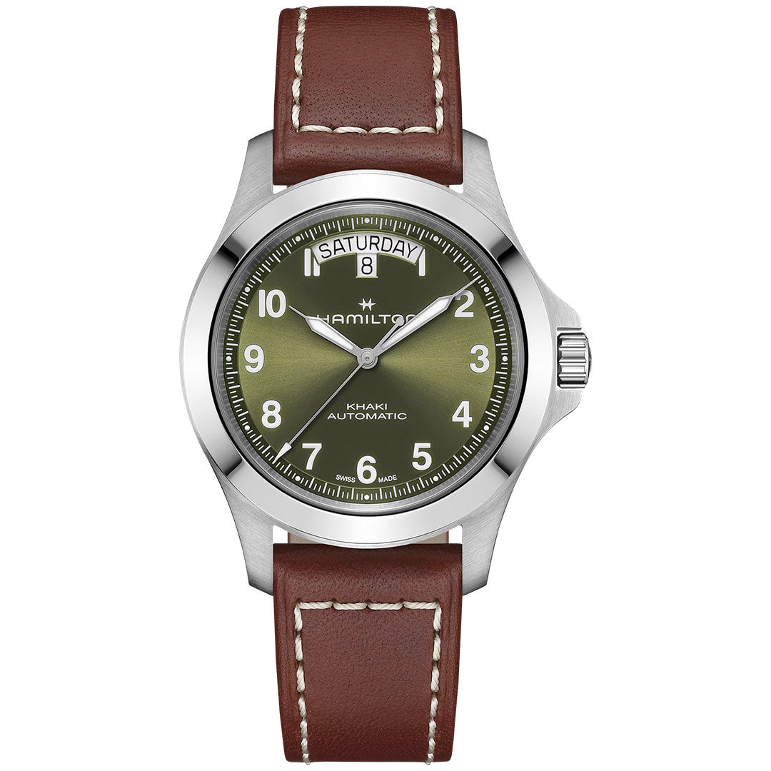 The Hamilton Khaki Field King Auto 40mm Watch by Hamilton Watch features an olive green dial with white numerals, day/date at 12 o’clock, a silver case, and a brown leather strap with white stitching in a classic military style.