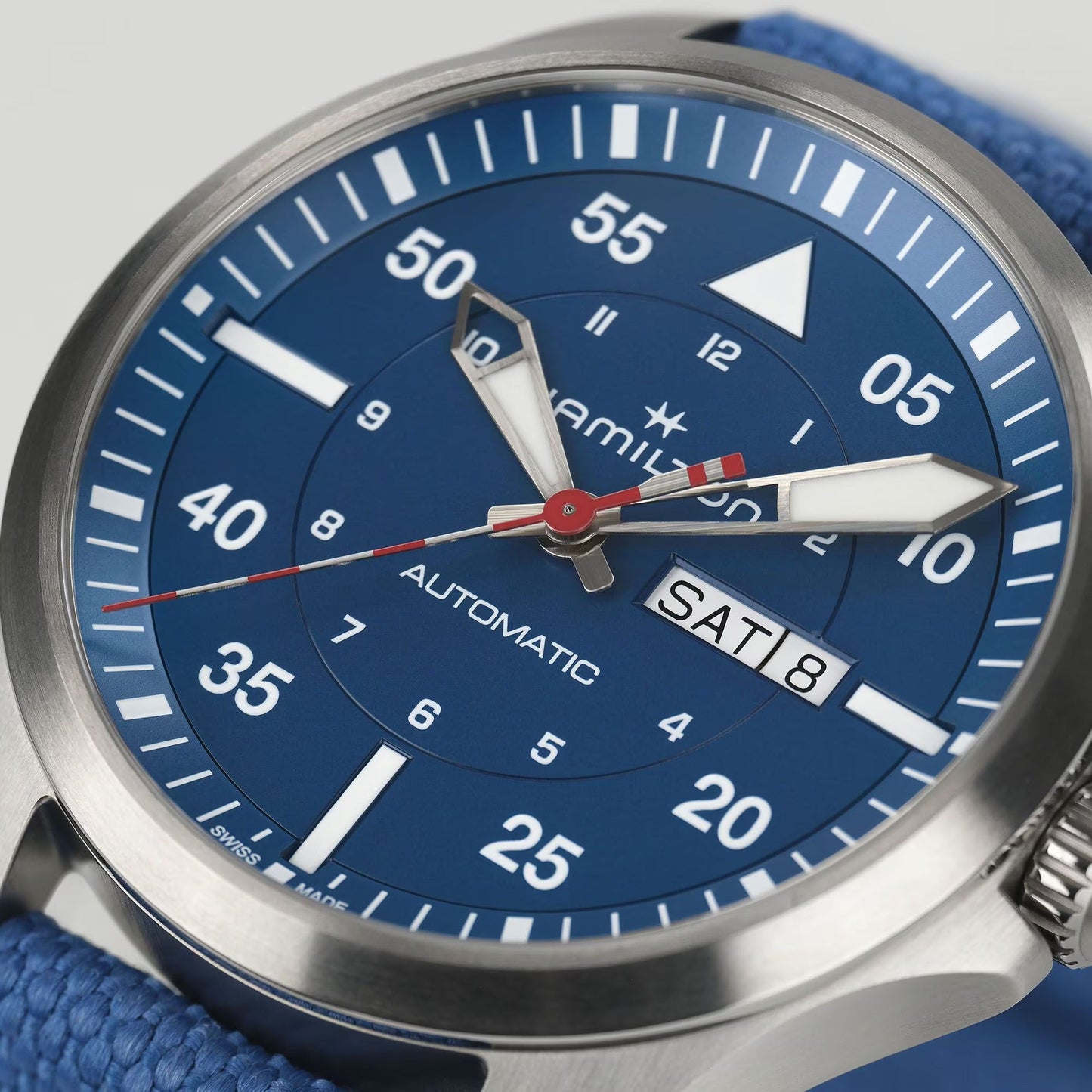 A close-up of the Hamilton Khaki Aviation Pilot Day Date Air Glaciers Edition Auto 42mm by Hamilton Watch, featuring a blue dial, white markers, titanium case, blue fabric strap, and H-30 automatic movement with day-date window.
