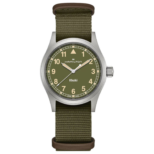 The Hamilton Khaki Field Quartz 38mm Watch by Hamilton Watch has a khaki green dial with beige numbers, a silver case, round face, olive green fabric strap, and displays "Hamilton" and "Khaki" on the dial.