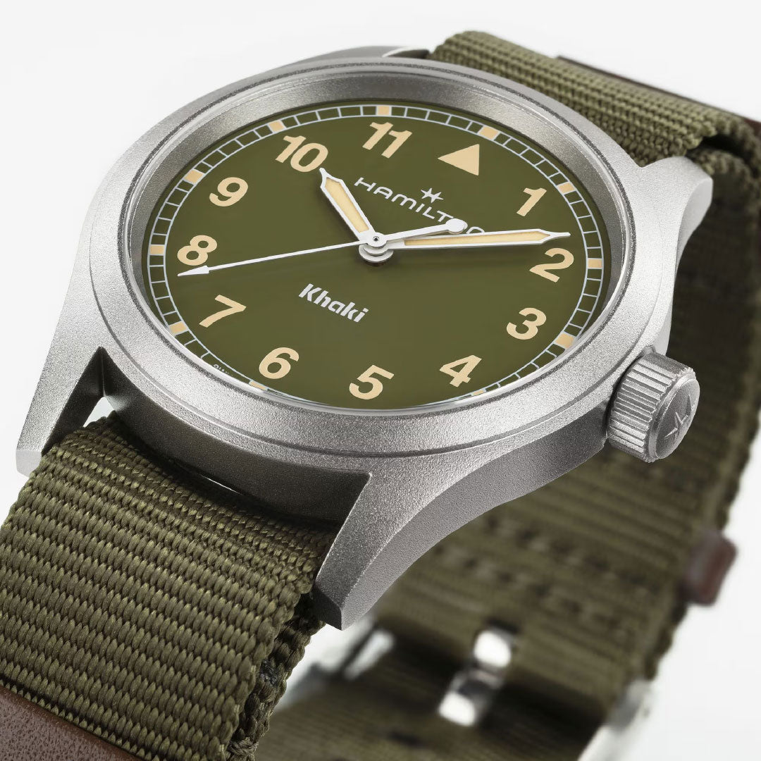 A close-up of the Hamilton Watch Khaki Field Quartz 38mm, featuring a khaki green dial, tan Arabic numerals, matching green fabric strap, and a matte silver case for a simple military-inspired look.