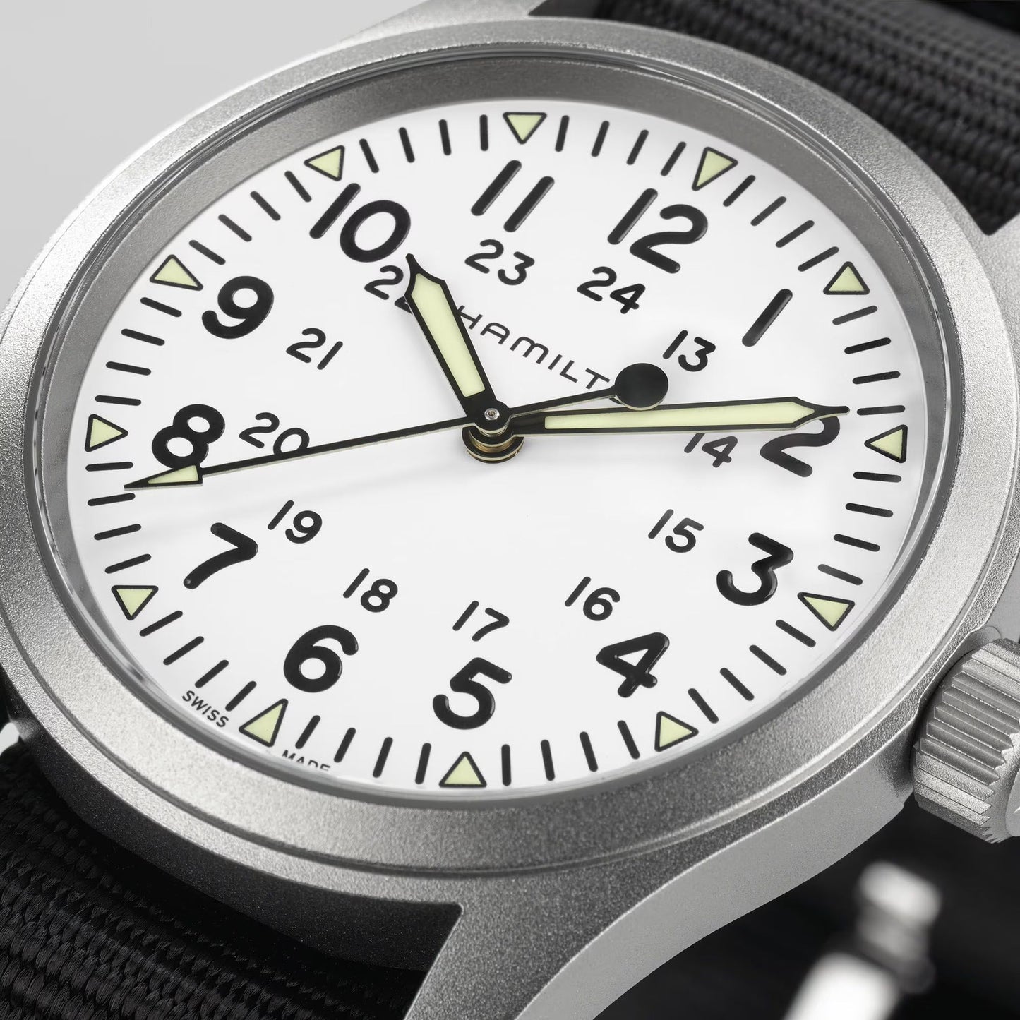 Close-up of the Hamilton Watch Khaki Field Mechanical 38mm, featuring a white dial with black numerals, 24-hour inner ring, luminous hands, and black NATO strap; stainless steel case; time displayed is about 8:14:30.