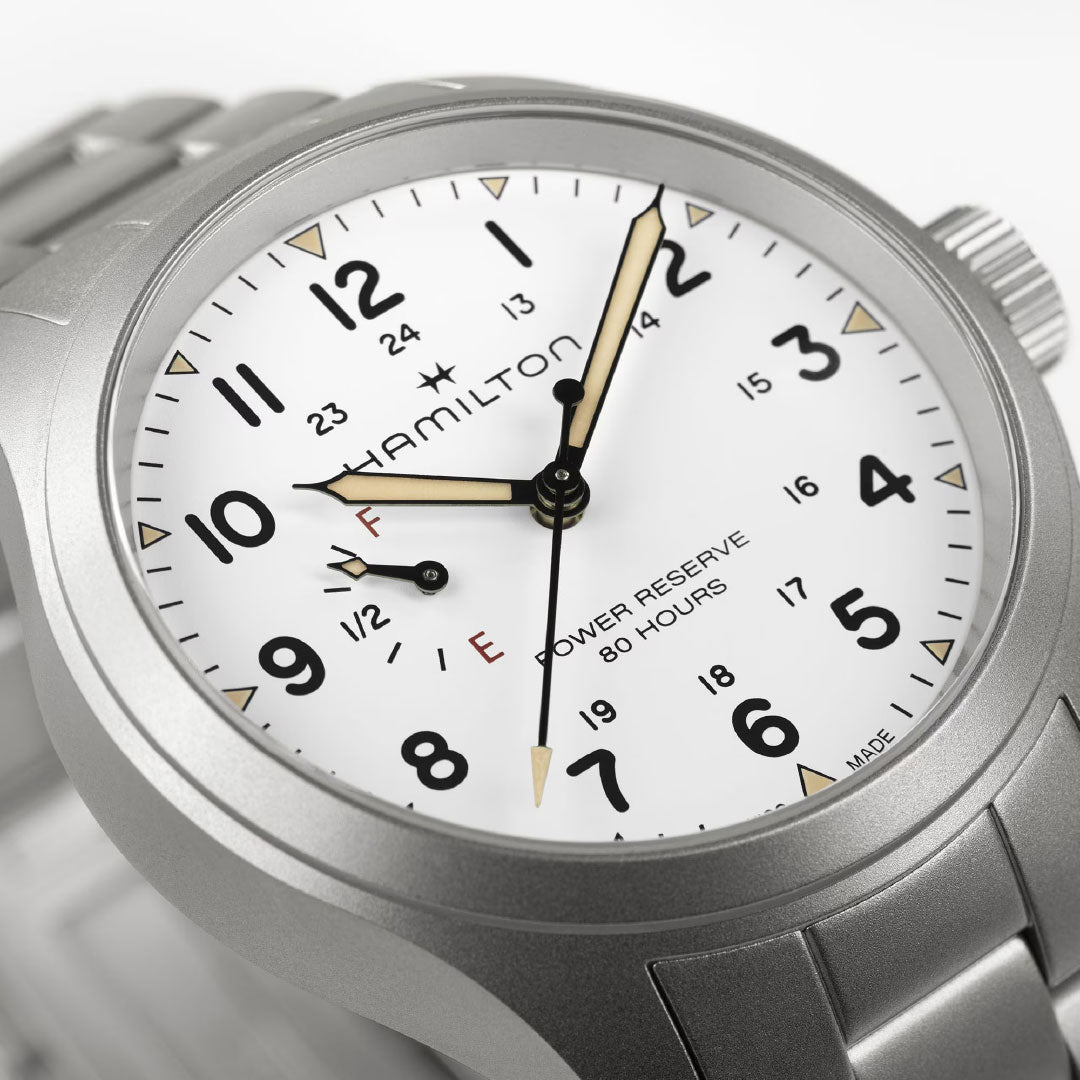 A close-up of the Hamilton Watch Khaki Field Mechanical Power Reserve 40mm, featuring a white dial, black numerals, gold-tone hands, 80-hour power reserve indicator, and stainless steel bracelet. The time reads 10:10:33.