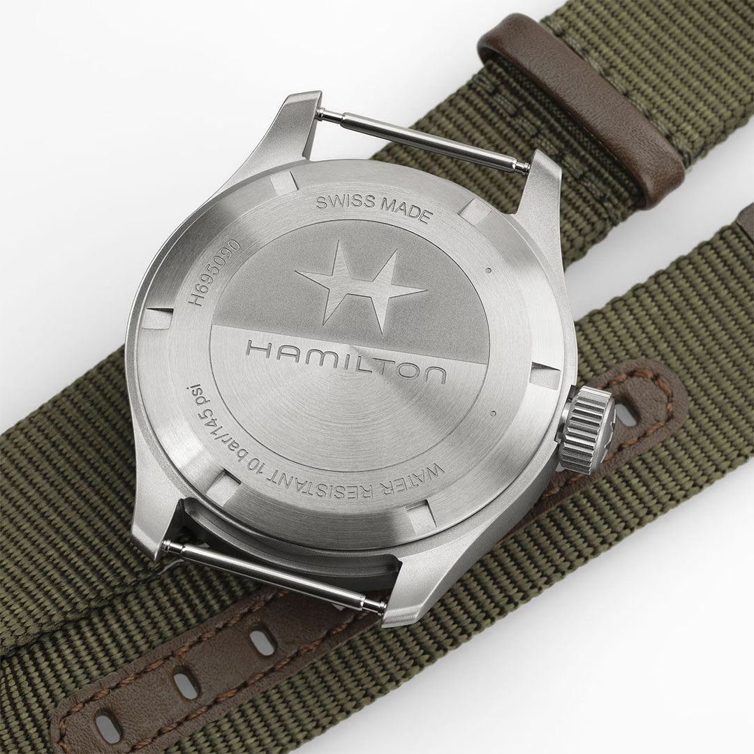 Close-up of the Hamilton Khaki Field Power Reserve Mechanical 40mm by Hamilton Watch, featuring an engraved stainless steel case and a green fabric strap with brown leather details. Swiss made, water resistant to 10 bar, with impressive power reserve.