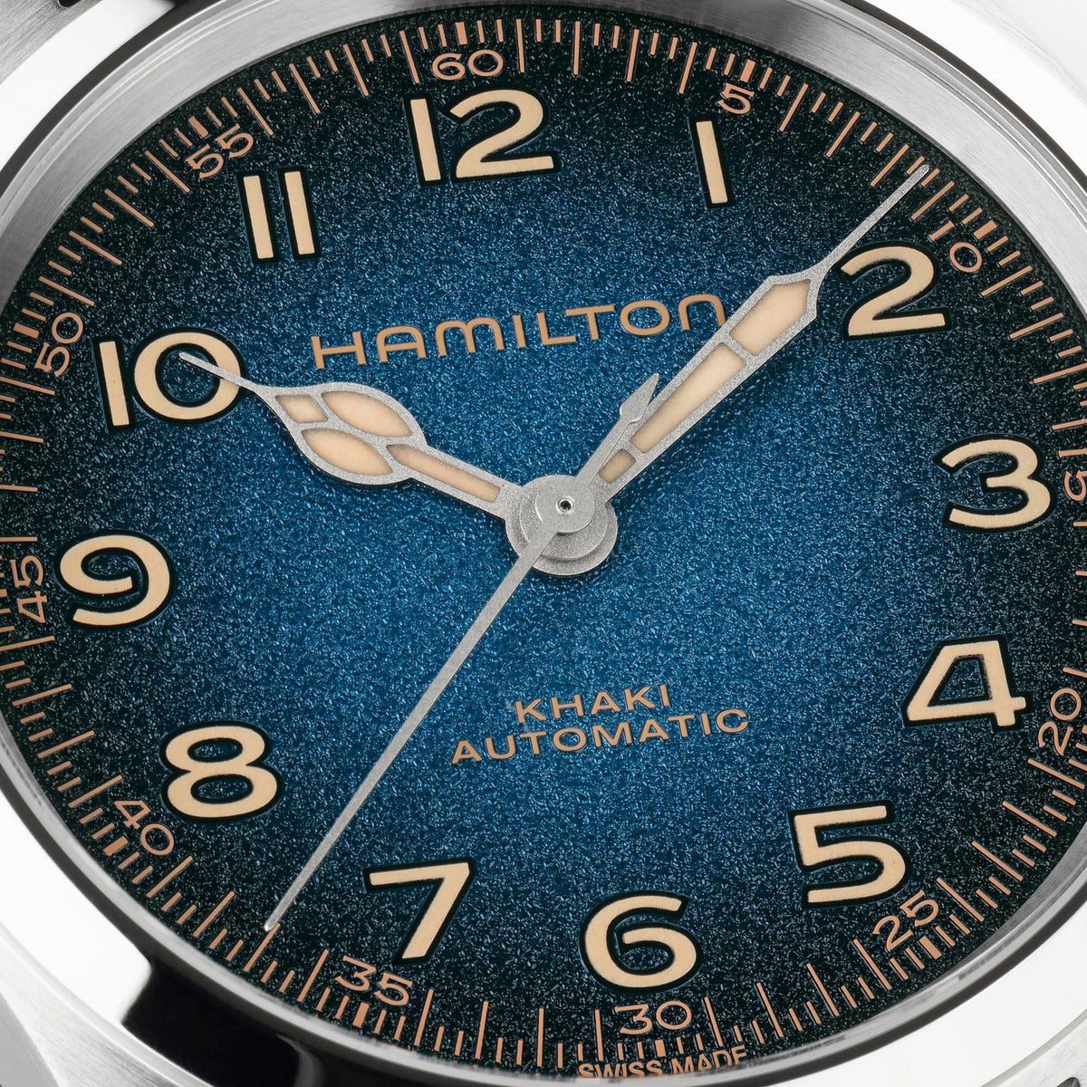 A close-up of the Hamilton Watch Khaki Field Murph Auto 38mm showcases its blue-to-black gradient dial with gold-tone numerals, hands, and markers, and a seconds hand pointing at 7. The partially visible “SWISS MADE” inscription along the bottom edge highlights a striking detail on this automatic model featuring an advanced calibre.