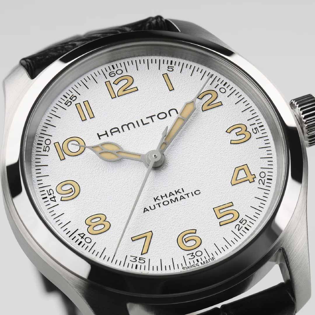 A close-up of the Hamilton Khaki Field Murph Automatic 38mm Watch showcases its vintage appeal. The silver case, white dial, and gold-toned numerals beautifully enhance the black leather strap. Emblazoned with the Hamilton Watch brand name on the dial, this timepiece captures classic charm in line with the iconic Murph model.