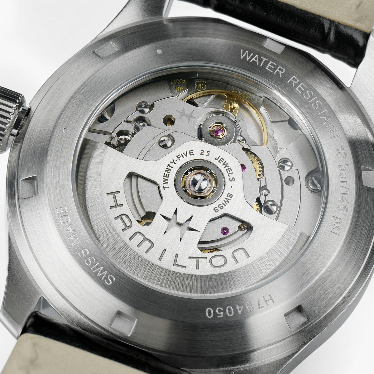Close-up of the Hamilton Khaki Field Murph Auto 38mm Watch’s transparent case back reveals the intricate automatic calibre in motion, showcasing visible gears and a rotor inscribed with “Hamilton.” Engravings highlight its water resistance and Swiss-made quality.