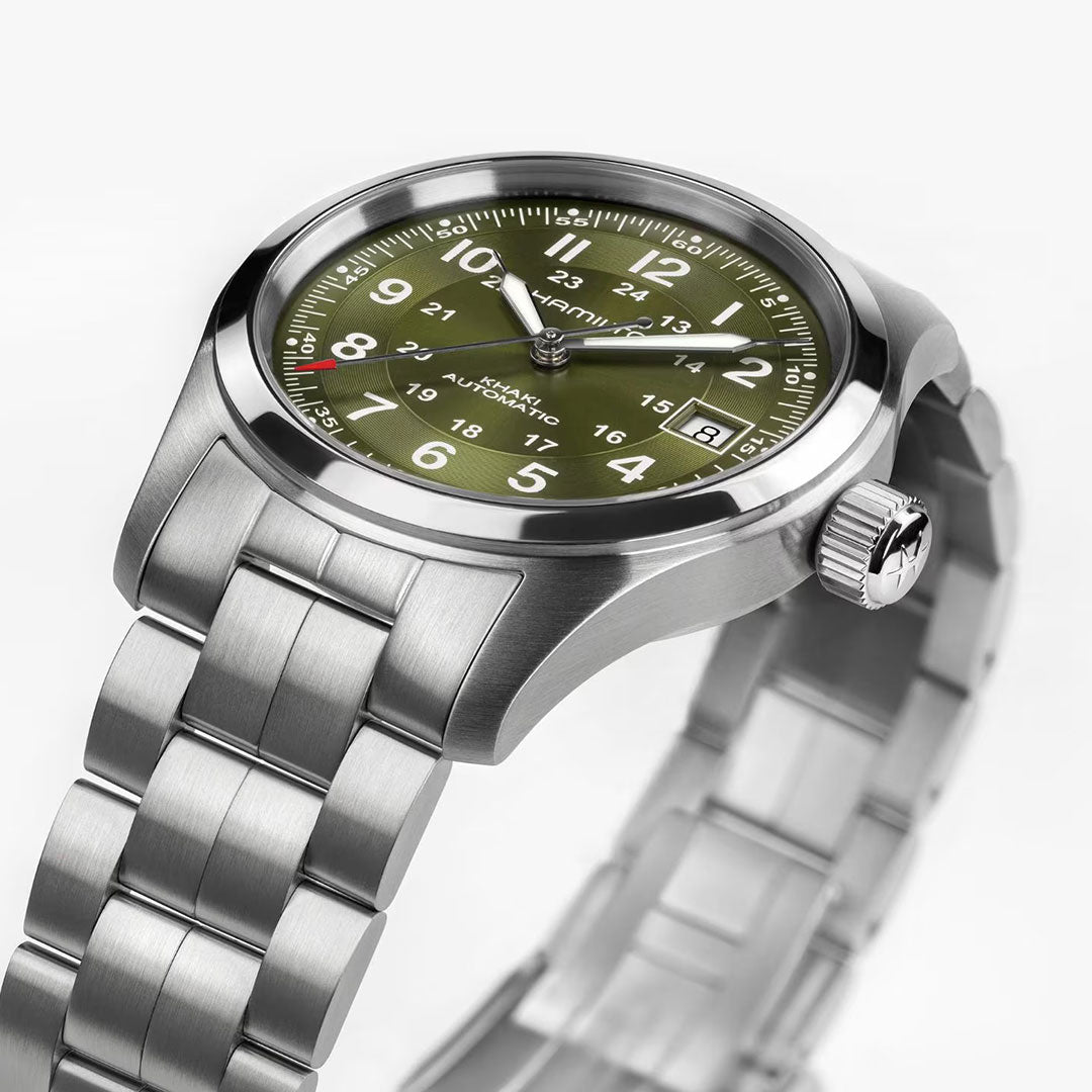 The Hamilton Khaki Field Auto 38mm Watch by Hamilton Watch features a stainless steel case, brushed metal band, olive green dial with white Arabic numerals, date window, silver hands, and a crown adorned with a star-shaped logo.