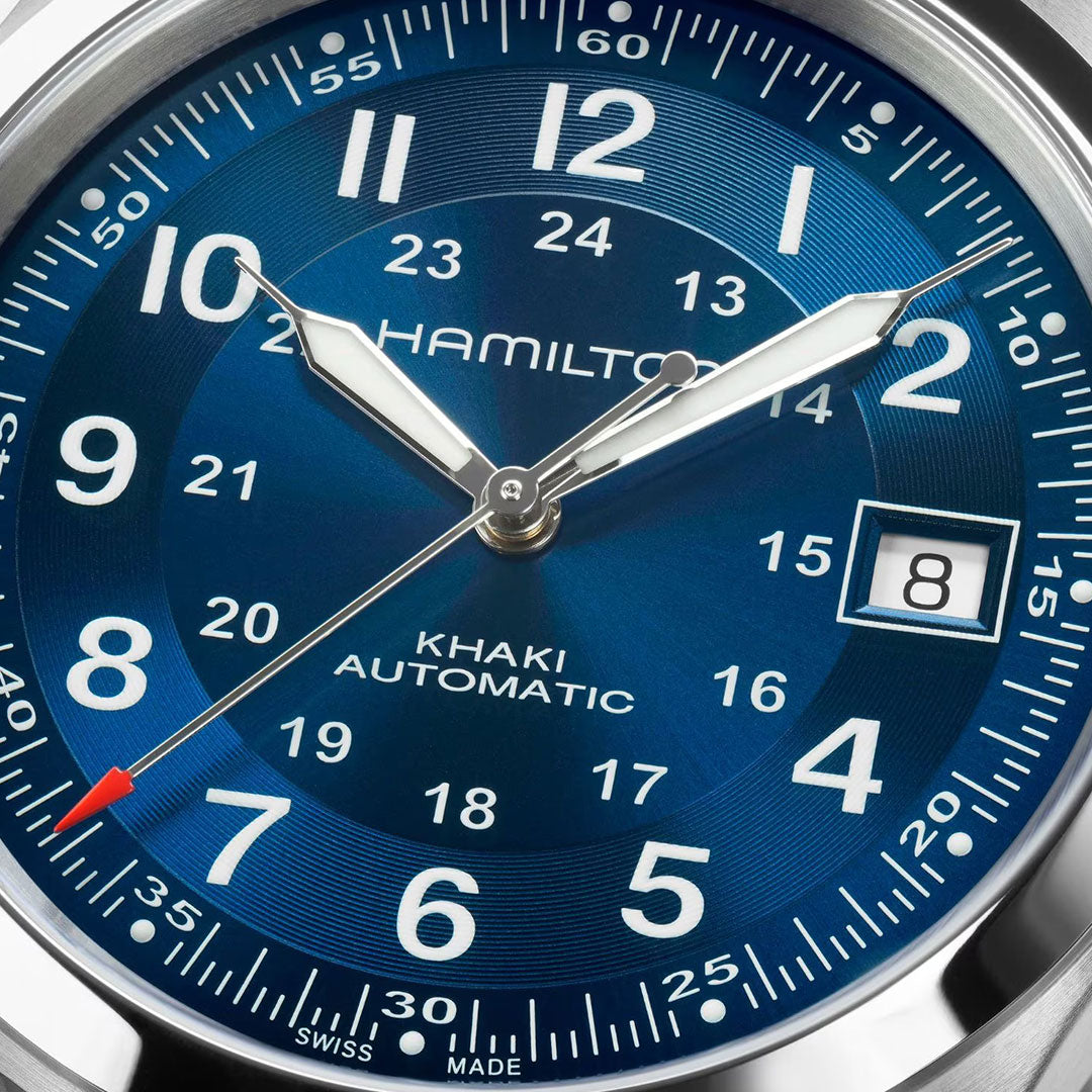 Close-up of the Hamilton Khaki Field Auto 38mm Watch by Hamilton Watch, featuring a blue dial with 12- and 24-hour markers, silver hands, H-10 automatic movement, date at 3 o’clock, and a red-tipped seconds hand.