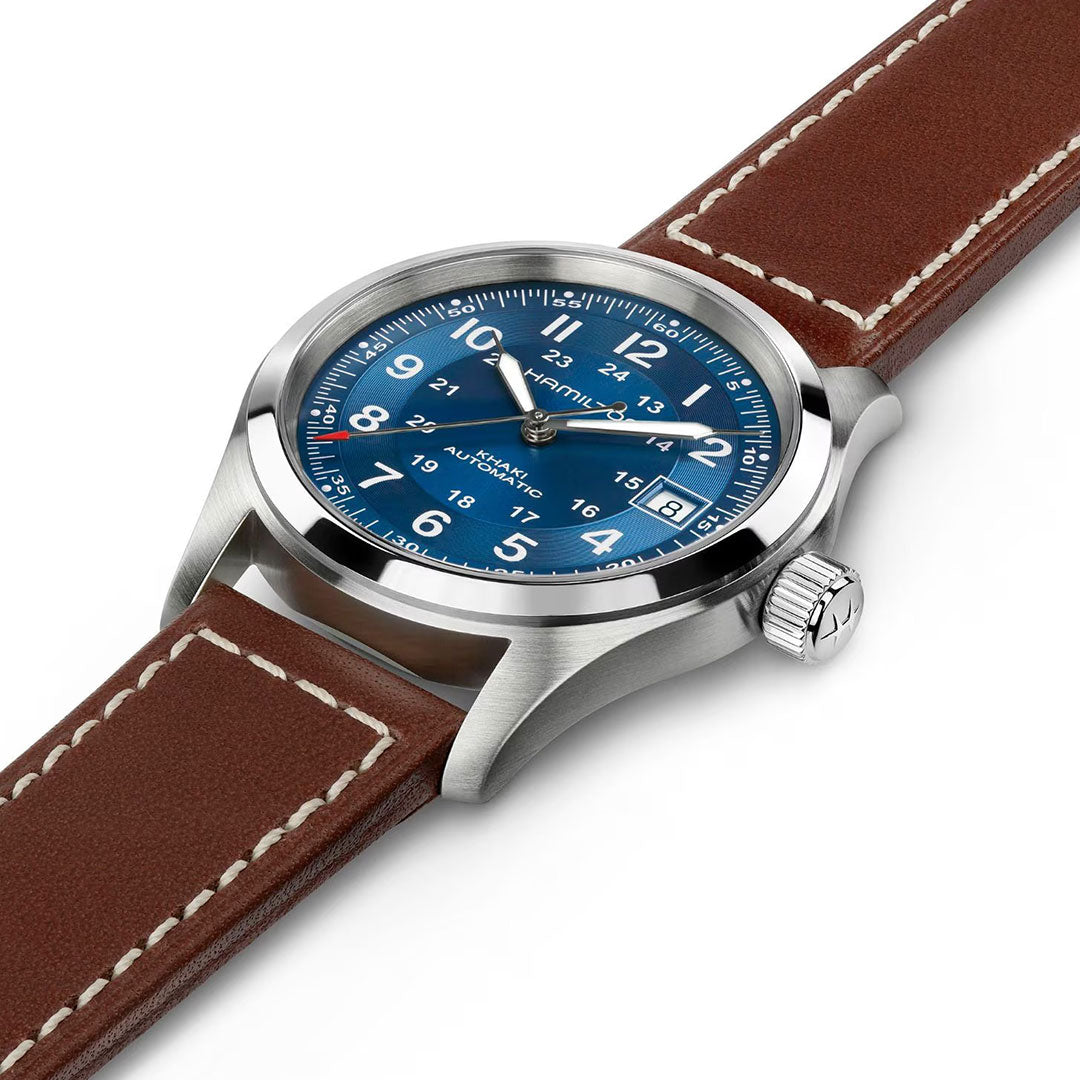 The Hamilton Khaki Field Auto 38mm Watch by Hamilton features a stainless steel case, blue dial with white numerals and date, and a brown leather strap with white stitching. Powered by the H-10 automatic caliber, it embodies true military heritage.