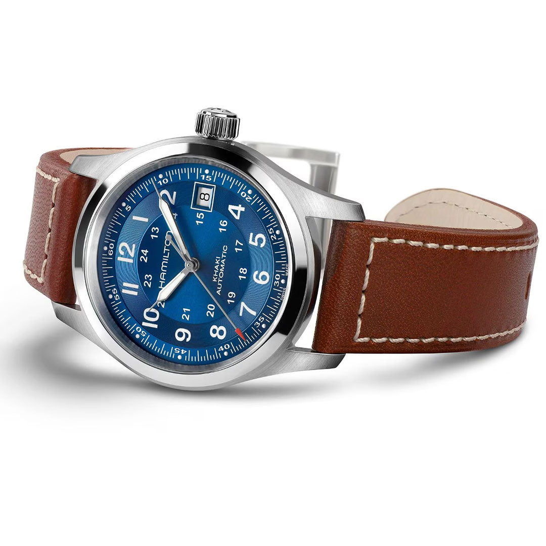 The Hamilton Khaki Field Auto 38mm Watch by Hamilton Watch features a stainless steel case, blue dial with white numerals, brown leather strap, and H-10 automatic movement with date at 3 o’clock, showcased at an angle on a white background.