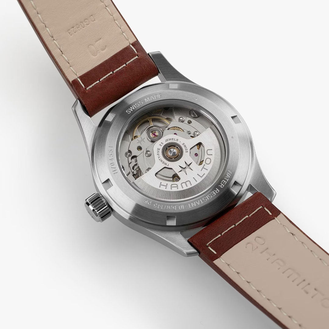 Close-up of the Hamilton Khaki Field Auto 38mm Watch by Hamilton Watch, showing the H-10 automatic movement through its transparent case back. It features a brown leather strap with beige stitching, echoing its military-inspired design.