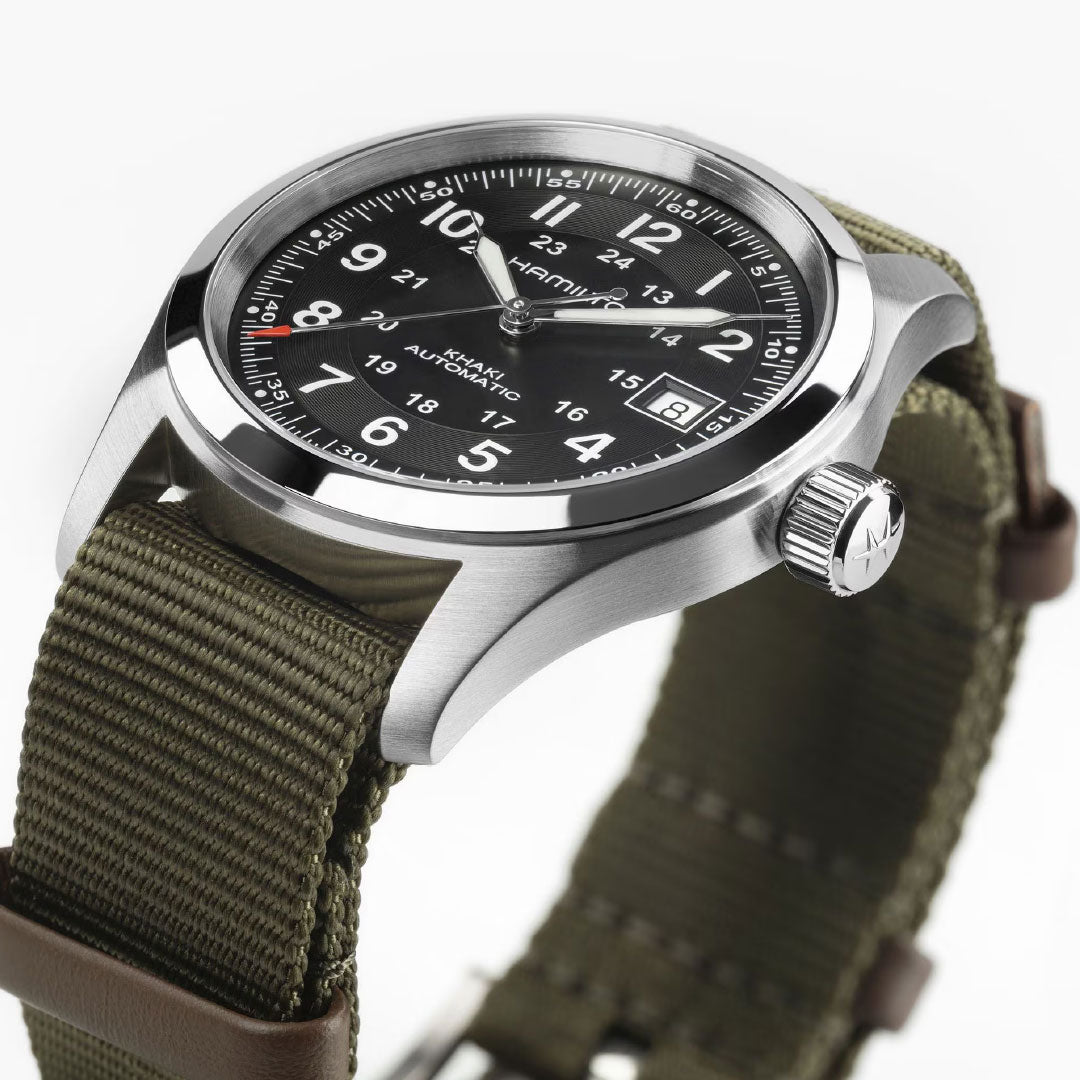 A close-up of the Hamilton Watch Khaki Field Auto 38mm Call of Duty edition, featuring a black dial with white markers, date window, olive green fabric strap, silver case with textured crown—Swiss-made precision and style.