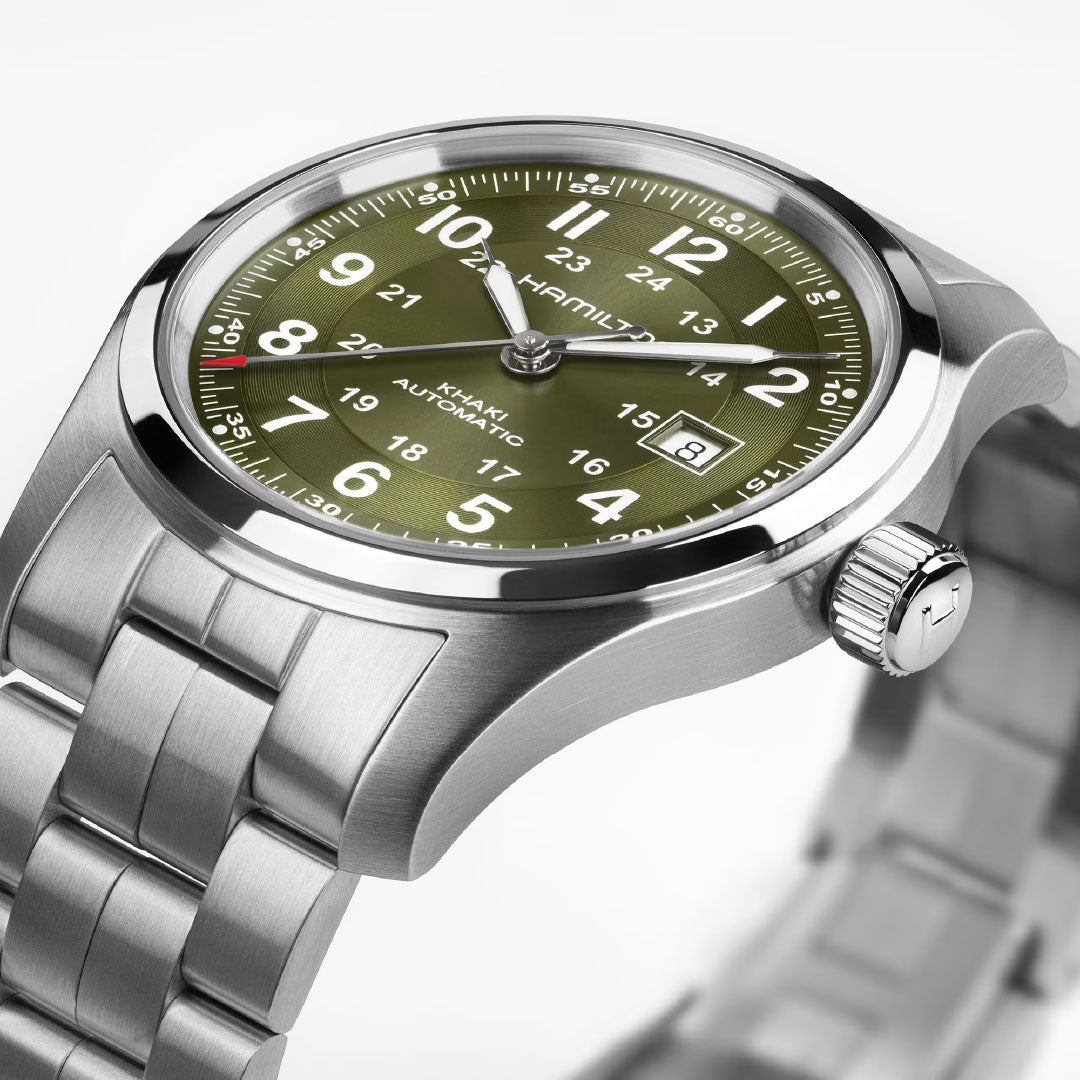 A close-up of the Hamilton Watch Khaki Field Auto 42mm features a green dial with white numerals, a silver stainless steel bracelet, red-tipped second hand powered by an automatic caliber, and a date window at 3 o’clock.