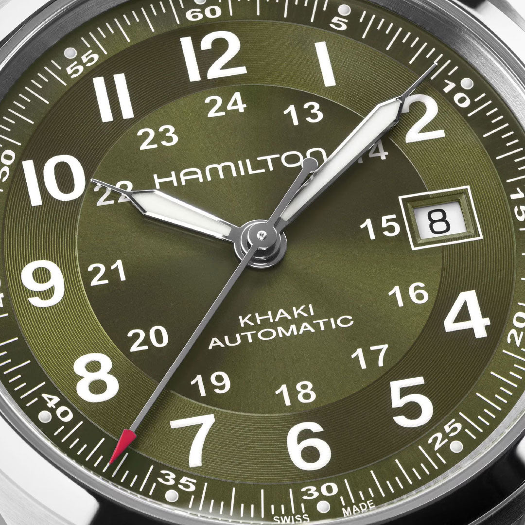 Close-up of a Hamilton Watch Khaki Field Auto 42mm face with an olive green background, white numerals, and a date window at 8. The watch hands display 12:08:37.
