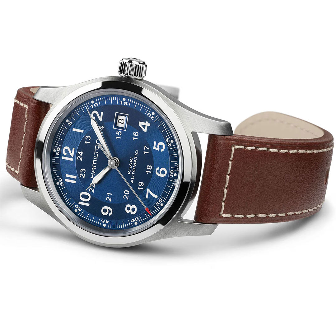 The Hamilton Khaki Field Auto 42mm Watch by Hamilton Watch features a blue dial, silver hour markers, H-10 automatic caliber, date at 3 o’clock, and a brown leather strap with white stitching, shown on a white background.