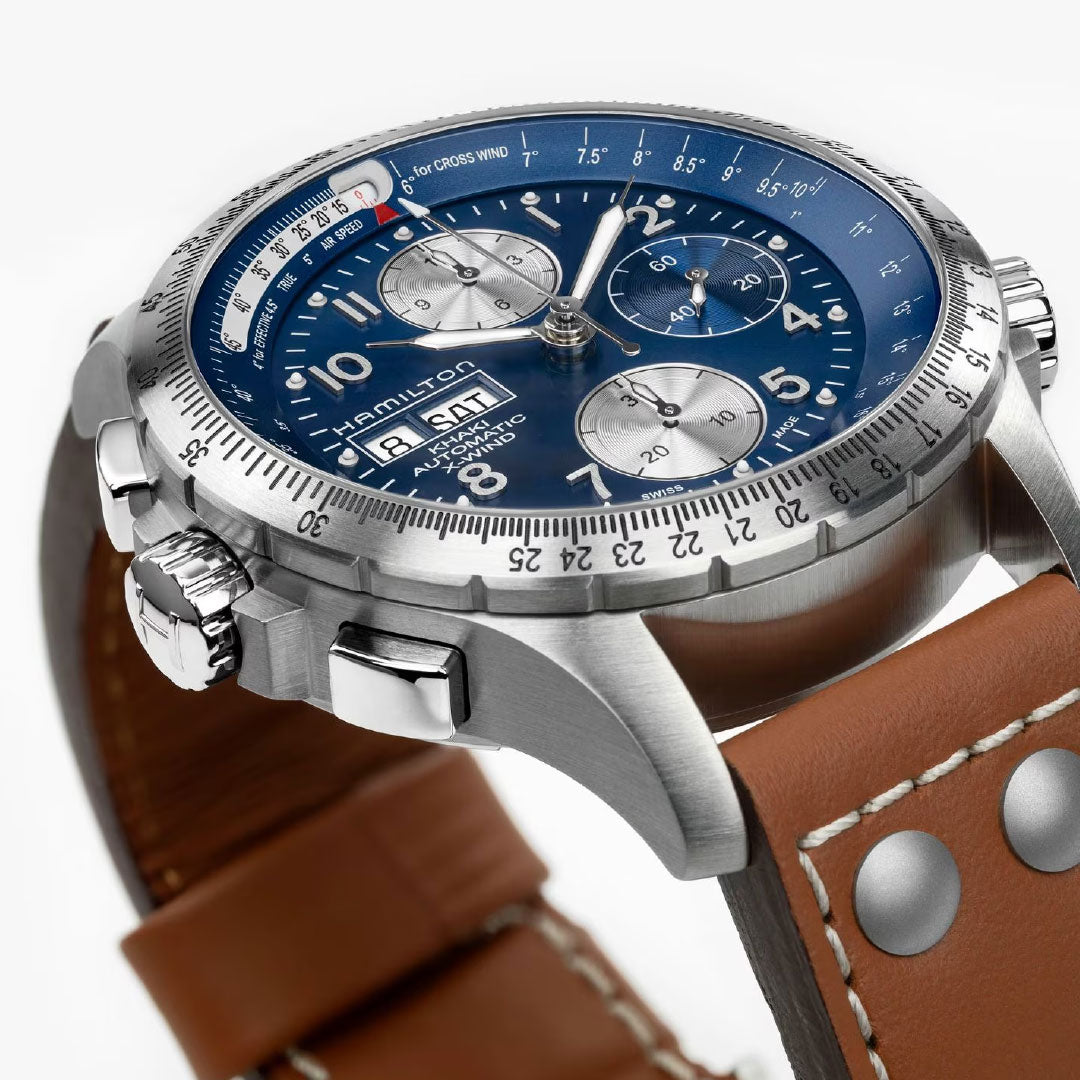 A close-up of the Hamilton Khaki Aviation X-Wind Auto Chrono 44mm watch by Hamilton Watch, featuring a blue dial, silver subdials, day-date display, and a brown leather strap with metal rivets.