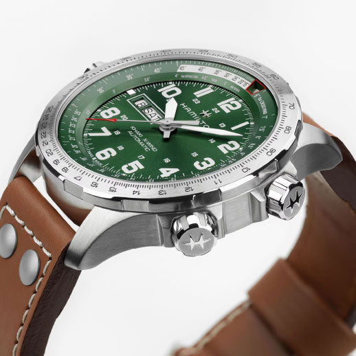 The Hamilton Khaki Aviation X-Wind Day Date Auto 45mm by Hamilton Watch features a green dial with white numbers, a stainless steel case, H-30 movement (80-hour reserve), brown leather strap, and two crown buttons with star designs.