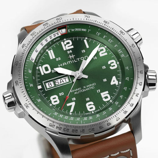 A close-up of the Hamilton Khaki Aviation X-Wind Day Date Auto 45mm Watch by Hamilton Watch, featuring a green dial, bold white numerals, a brown leather strap, day-date display at 9 o’clock, and an 80-hour power reserve.