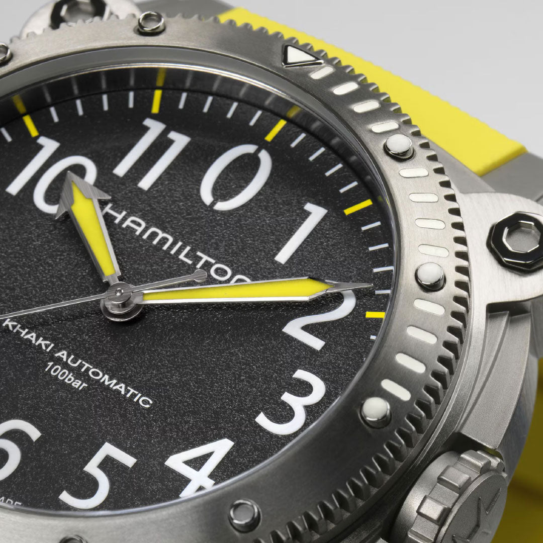 Close-up of the Hamilton Khaki Navy BeLow Zero Auto Titanium 46mm Watch by Hamilton Watch, featuring a textured black dial with large white numerals, yellow accents, and a rugged stainless steel bezel with prominent screws and helium escape valve.