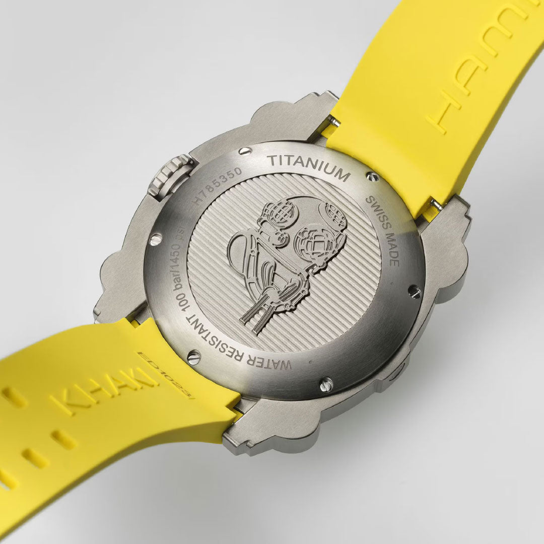 The Hamilton Khaki Navy BeLow Zero Auto Titanium 46mm Watch by Hamilton Watch features a titanium case back, bright yellow strap, diving helmet engravings, and "TITANIUM," "SWISS MADE," and "WATER RESISTANT 100M" text—a bold marine watch for underwater adventures.