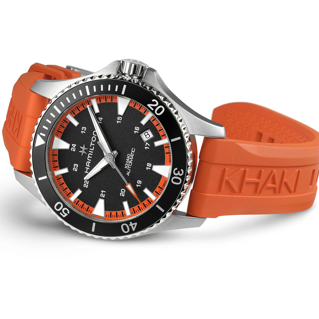 The Hamilton Khaki Navy Scuba Auto 40mm Watch by Hamilton Watch features a black dial, white markers, and a tangerine orange strap embossed with "KHAKI." Displayed at an angle, it has a black bezel with white numerals.