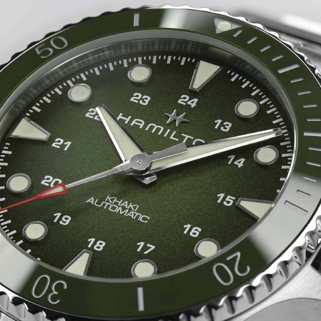 Close-up of the Hamilton Khaki Navy Scuba Automatic 43mm Watch by Hamilton Watch, showcasing a green dial accompanied by a ceramic bezel. It boasts white hour markers and luminescent hands, with the second hand accented in red. Powered by the precise H-10 automatic movement, its bezel is detailed with minute indicators.