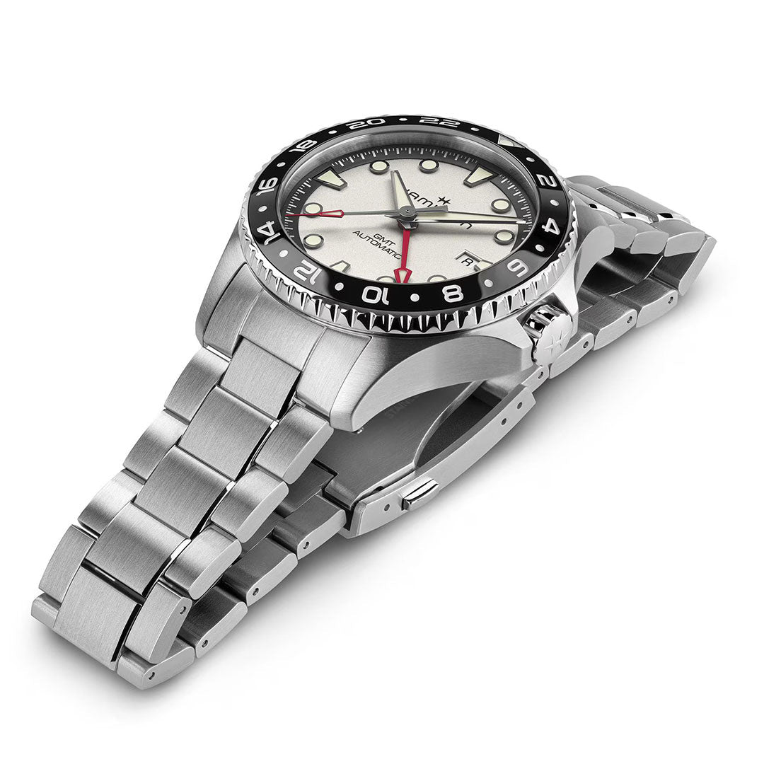 The Hamilton Khaki Navy Scuba Auto GMT 43mm by Hamilton Watch features a stainless steel case, silver bracelet, beige dial, black and red 24-hour bezel, and luminous hour markers. The watch is angled to showcase its dial and band.