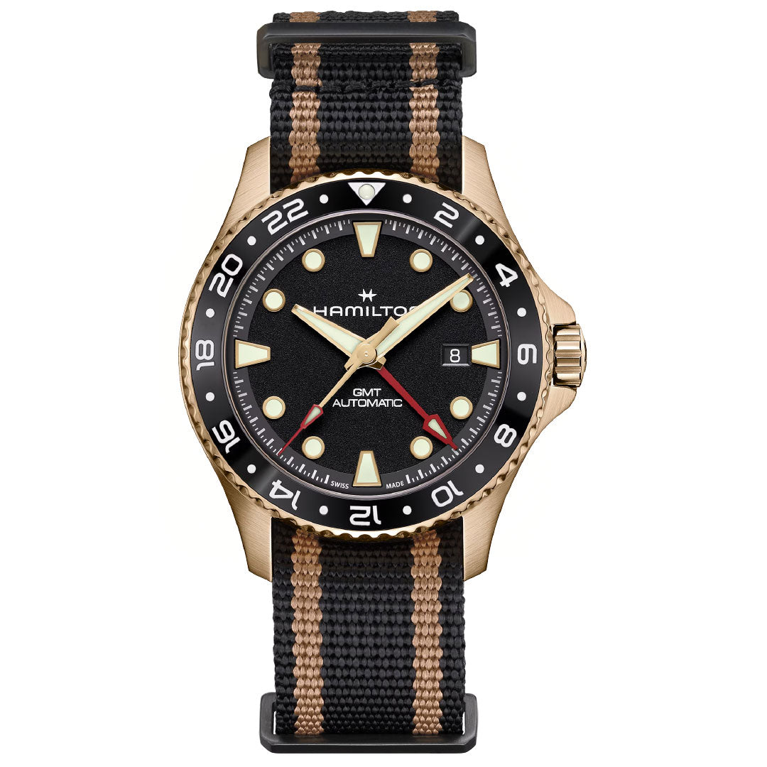 The Hamilton Khaki Navy Scuba Automatic GMT 43mm Bronze Watch by Hamilton Watch features a black and bronze bezel, black dial, bold markers, and a black fabric strap with beige stripes. Red and white accents highlight its multiple time zone tracking.