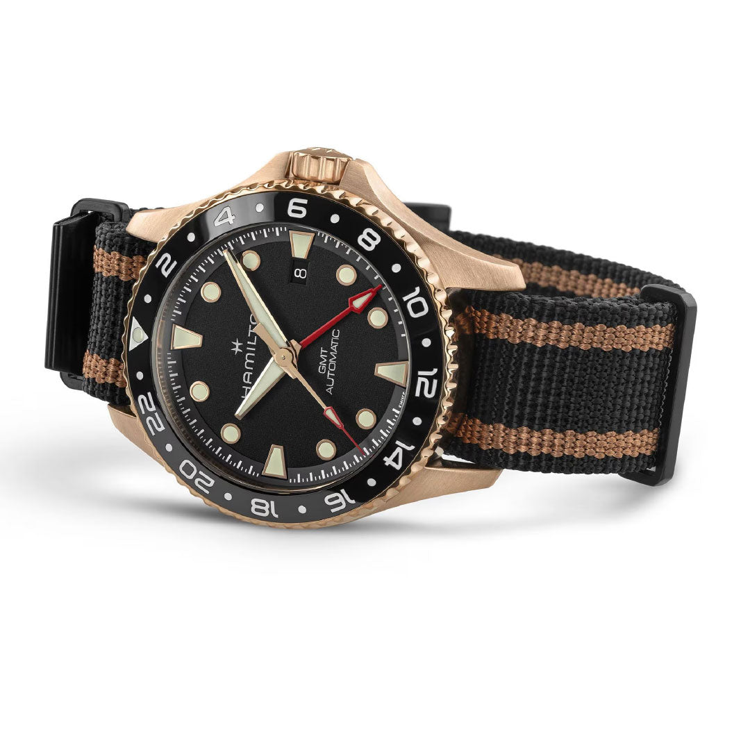 The Hamilton Khaki Navy Scuba Automatic GMT 43mm Bronze Watch by Hamilton Watch features a bronze case, black dial, gold and white markers, striped NATO strap, and a 24-hour rotating bezel—perfect for travelers tracking multiple time zones.