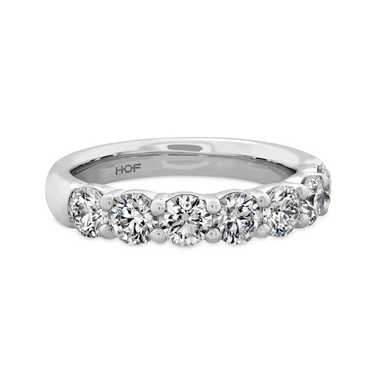 The Hearts On Fire Signature 18K White Gold Round Brilliant Diamond Anniversary Ring, crafted by Hearts on Fire, showcases a polished silver band adorned with a row of seven radiant round-cut diamonds. These premium diamonds feature SI-VS clarity for exceptional brilliance, standing out beautifully against the white gold backdrop.