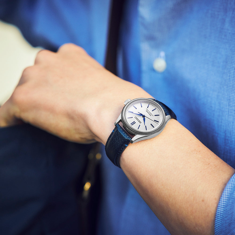 A Seiko Presage Classic Series 145th Anniversary Limited Edition Automatic With Manual Winding 36mm Watch with a white textured dial, blue hands, and a dark blue leather strap worn on a wrist.