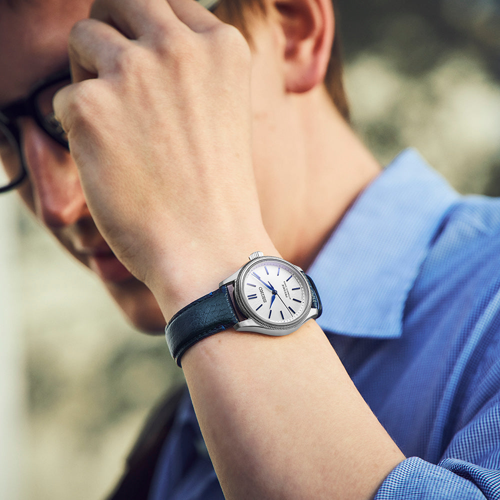 A person wearing a Seiko Presage Classic Series 145th Anniversary Limited Edition Automatic With Manual Winding 36mm Watch with a white dial, blue hands, and a dark leather strap on their wrist.