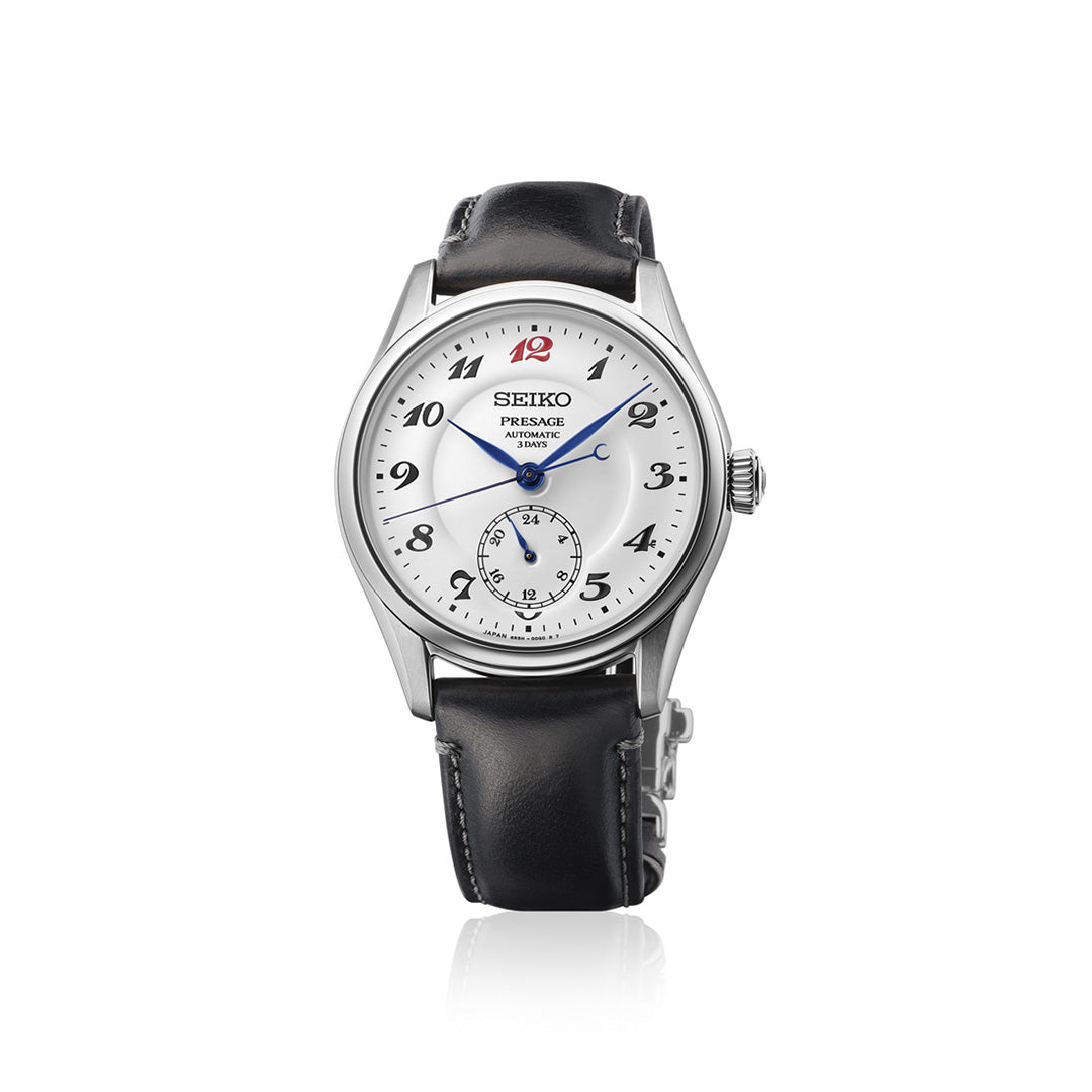Introducing the Seiko Presage Classic Series Automatic 39.6mm Watch by Seiko, featuring a silver-tone stainless steel case, elegant white dial with blue hands, black Arabic numerals, and a small seconds subdial positioned above 6 o’clock. The numeral 12 stands out in red for a distinctive touch, while the classic black leather strap completes its timeless style.