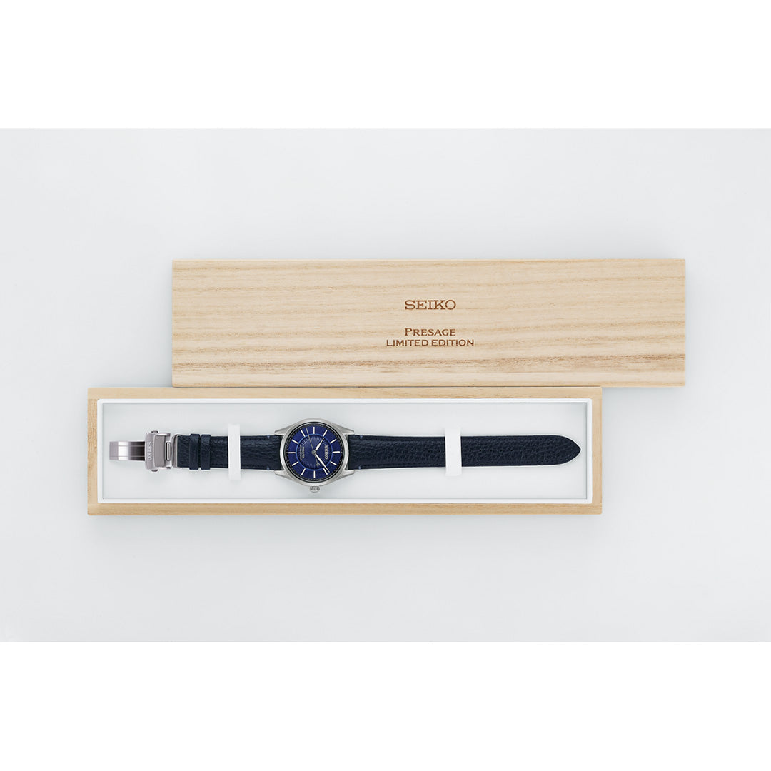 The Seiko Presage Classic Series 145th Anniversary Automatic 39.6mm Watch, a limited edition of only 1,500 pieces, is elegantly presented in an open light wood box. Featuring a blue face and black strap, this remarkable Seiko timepiece showcases refined craftsmanship and timeless design.